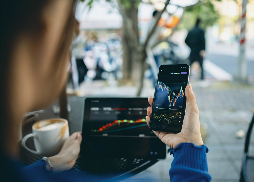 A picture of woman looking at stock on her phone and laptop.